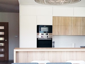 Biała kuchnia z drewnem - Średnia z salonem biała z zabudowaną lodówką kuchnia dwurzędowa, styl nowoczesny - zdjęcie od Biuro projektowe "Patio" Ewa Szymczak