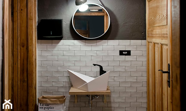 białe kafelki, asymetryczna umywalka, okrągłe lustro, drewniane drzwi