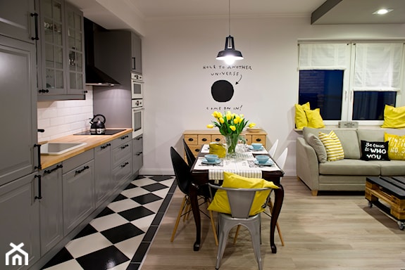 szare szafki kuchenne, żółte poduszki, czarno-biała podłoga, dekoracyjny napis na ścianie