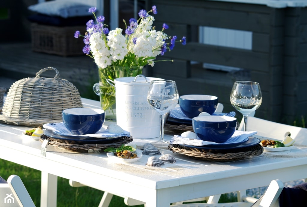 biały stół w ogrodzie, granatowa zastawa, szklany wazon ze świeżymi kwiatami