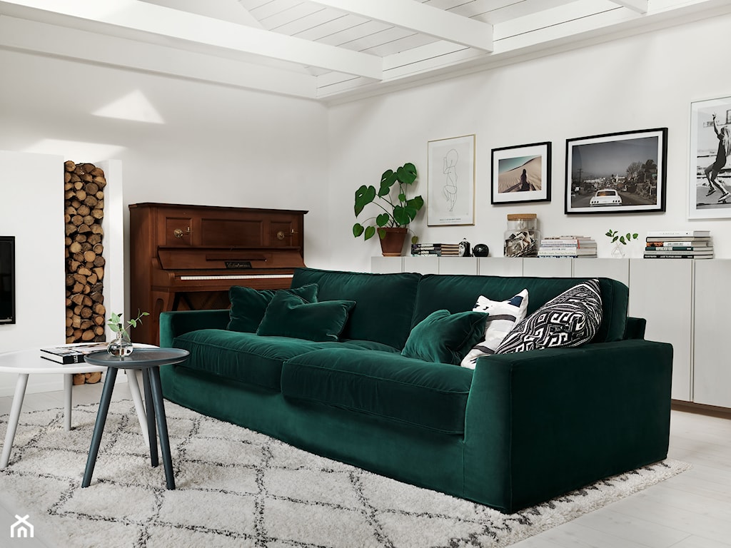 szmaragdowa sofa, drewniane pianino, białe ściany, rośliny doniczkowe w salonie