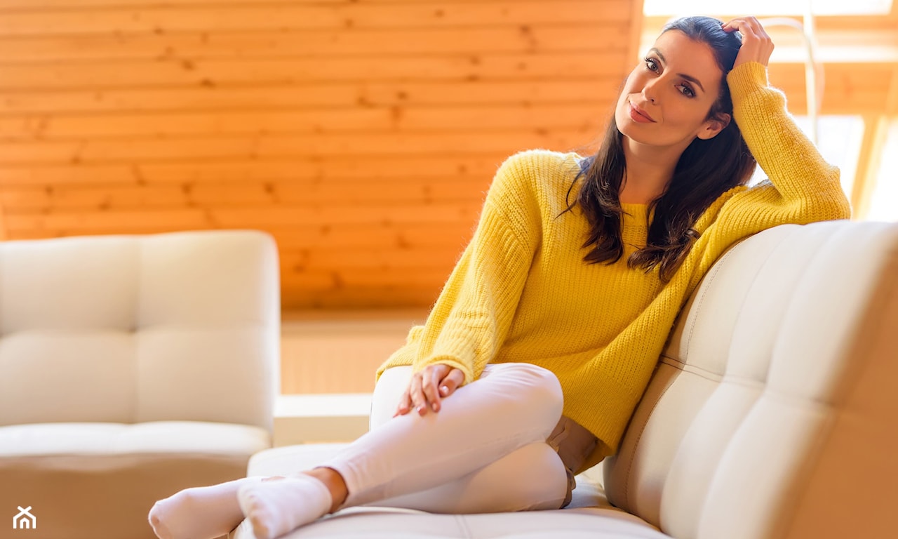 Kobieta w żółtym swetrze relaksuje się na beżowej sofie 