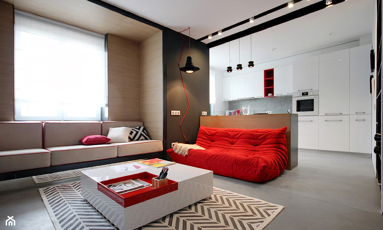 minimalistyczny salon połączony z kuchnią, białe meble kuchenne, czerwona sofa, biały stolik z połyskiem dywan w jodełkę