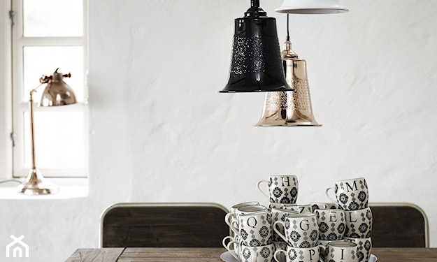 miedziana lampa wisząca, drewniany stół, białe filiżanki z czarnym wzorem
