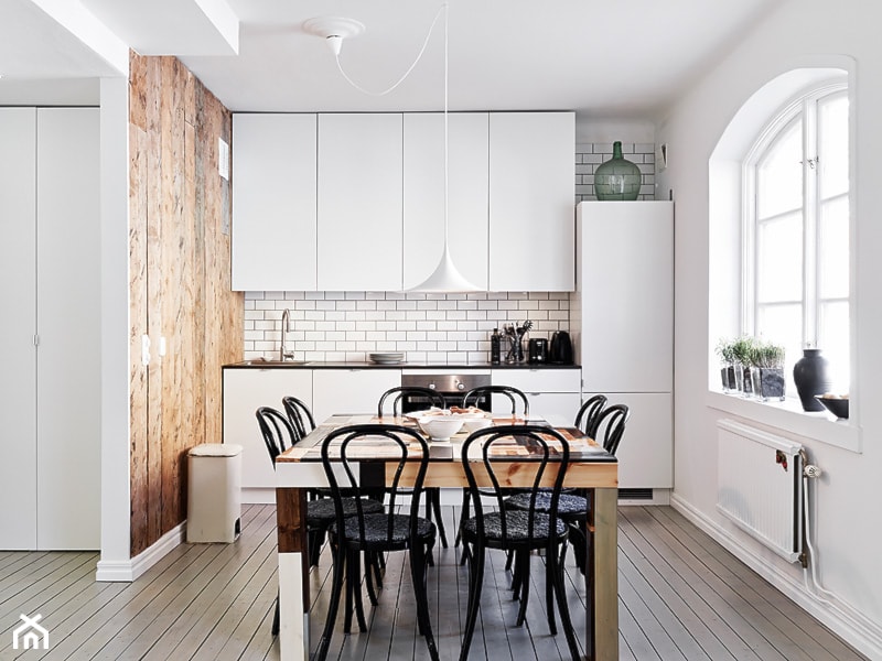 drewniana ściana w kuchni, czarne krzesła, białe meble, metalowa lampa wiszaca