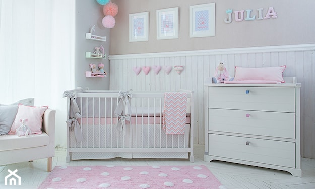 różowy dywanik w białe kropki, biała lamperia, biała komoda, białe łóżeczko dziecięce z różowym materacem
