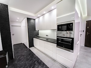 Mała otwarta biała czarna z zabudowaną lodówką z podblatowym zlewozmywakiem kuchnia jednorzędowa z kompozytem na ścianie nad blatem kuchennym, styl minimalistyczny - zdjęcie od Maldekor Mariusz Gąsiorowski