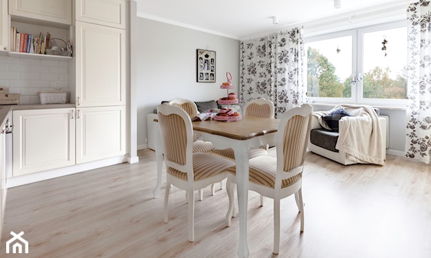 salon i kuchnia inspirowane stylem prowansalskim, beżowe meble kuchenne ze żłobieniami, drewniana podłoga, białe krzesła z beżowym obiciem