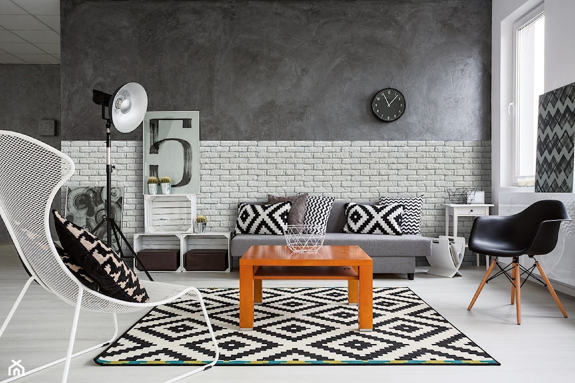 skandynawski salon z szara sofą z białą cegłą na ścianie