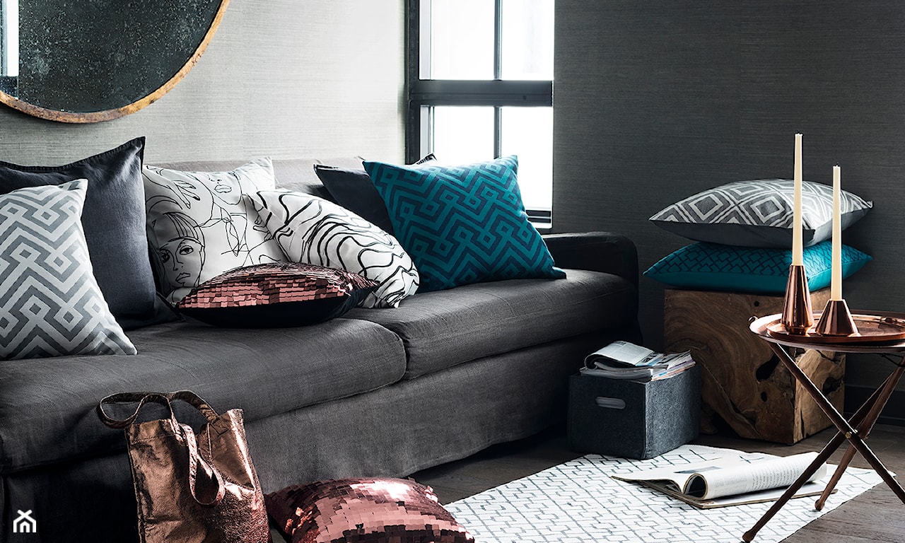 szara sofa, okrągłe lustro ścienne z drewnianą ramą, poduszki z cekinami, niebieskie poduszki