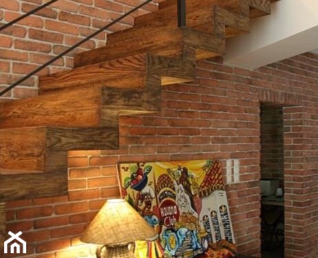 ceglana ściana, drewniane schody z metalową balustradą, lampa stołowa z beżowym abażurem