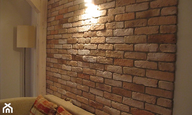 ceglana ściana z cegły, beżowa sofa, lampa podłogowa z białym abażurem