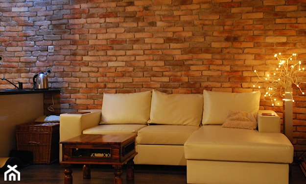 ceglana ściana w mieszkaniu, kremowy narożnik, drewniany stolik kawowy