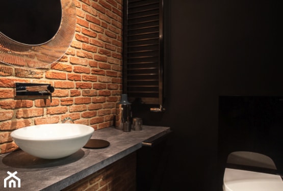 ceglana ściana w łazience, okrągłe lustro, betonowy blat pod umywalką