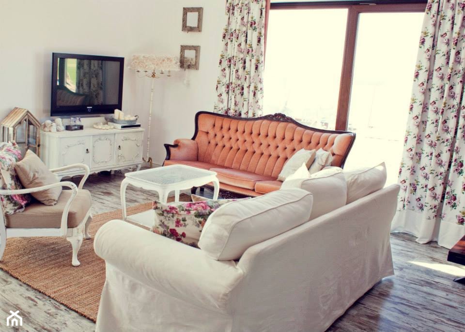 biała sofa, pomarańczowa sofa, białe zasłony w kwiaty, beżowy dywan z plecionki