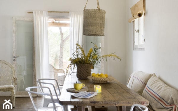 wiklinowy abażur lampy wiszącej, białe metalowe krzesła, stół z drewnianych desek, białe firany do podłogi, słomkowe rolety