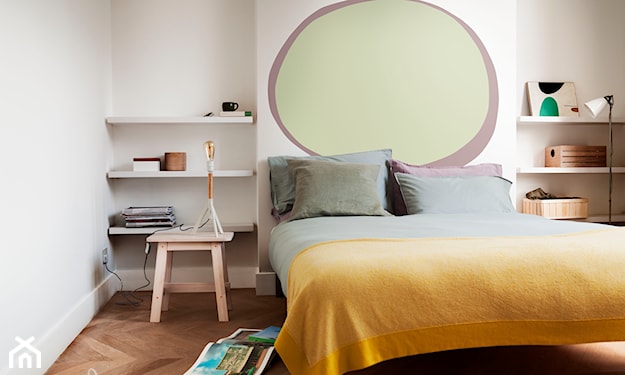 żółta narzuta na łóżku, kremowa ściana, drewniany taboret, białe półki