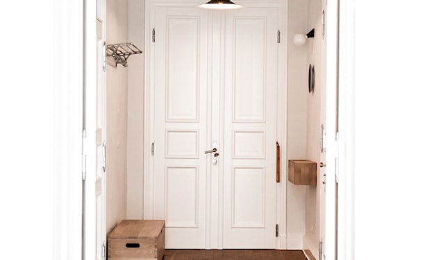 białe drzwi dwuskrzydłowe, czarna lampa wisząca, podłoga z ciemnego drewna, drewniana skrzynia