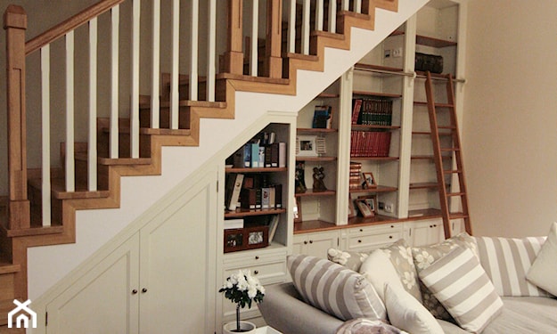 drewniane schody z balustradą, biała szafa pod schodami, szara sofa, poduszki w paski