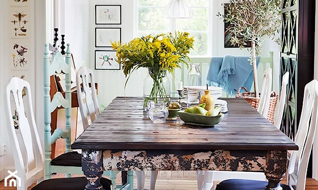 drewniany stół z nogami w kwiaty, szklany wazon, białe krzesła, metalowe lampy wiszące