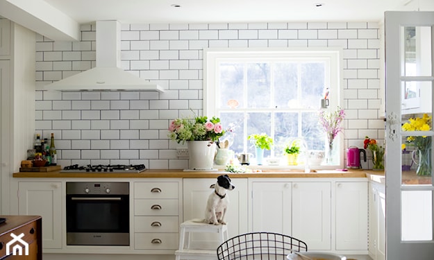 białe płytki na ścianie w kuchni, białe meble kuchenne, drewniany blat, druciane krzesło