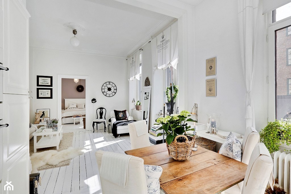 salon w stylu skandynawskim, podłoga z białych desek, drewniany stół, wiklinowy kosz, białe zasłony rzymskie