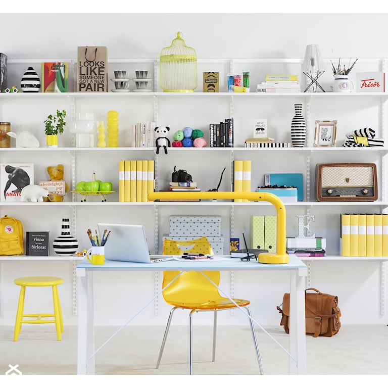 żółte krzesło, żółty stołek, białe biurko ze szklanym blatem, półki na ścianie, przedmioty ustawione na półkach, żółta lampa na biurku