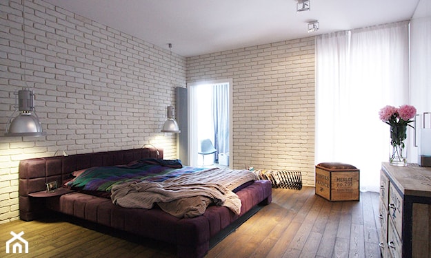 biała cegła w sypialni, drewniana podłoga, drewniana skrzynia, metalowa lampa podłogowa, fioletowe łóżko