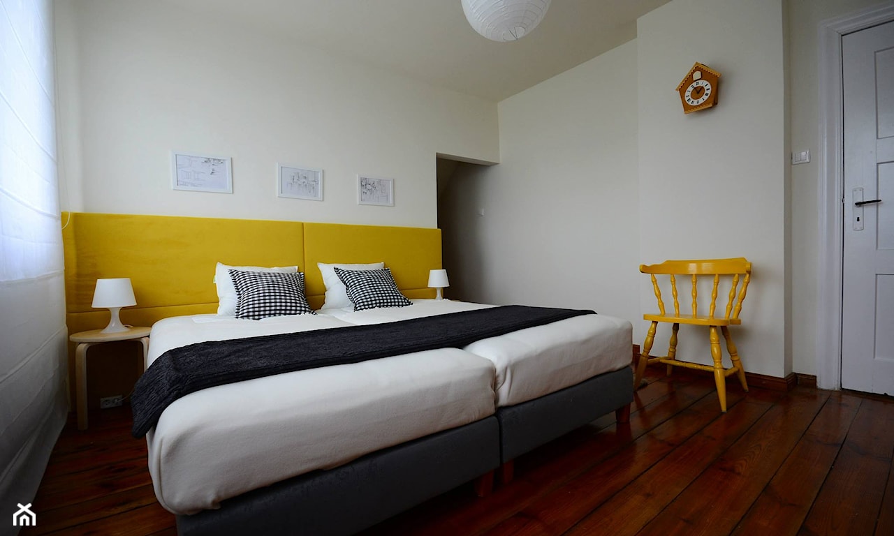 żółty zagłówek, podłoga z ciemnego drewna, żółte krzesło, grafitowa narzuta na łóżko