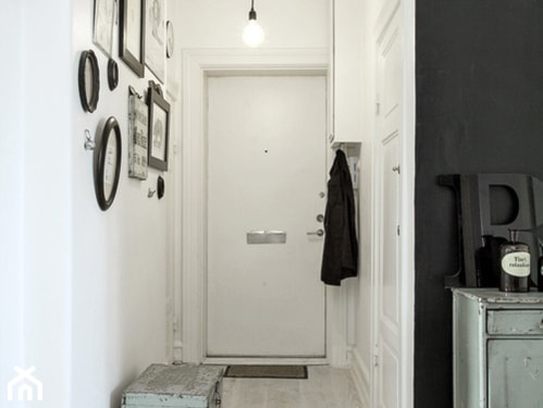 białe ściany w korytarzu, czarna ściana, małe obrazy w szerokich ramach