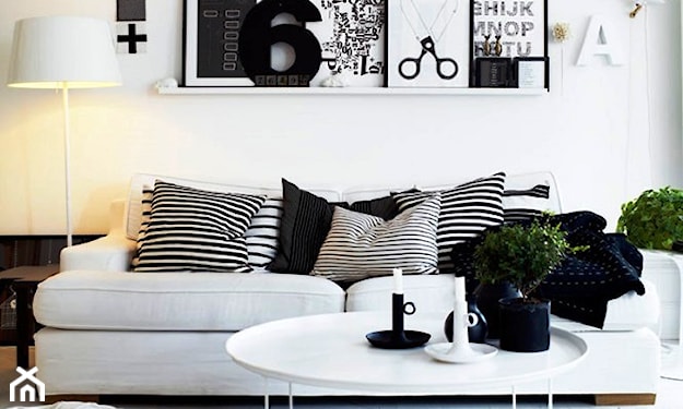 biało-czarny salon, biała sofa, poduszki w paski, lampa podłogowa z białym abażurem, dekoracja ścienna z biało-czarnych grafik