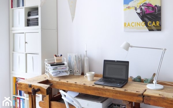 drewniane biurko, biała lampa biurowa, kolorowy plakat ozdobny