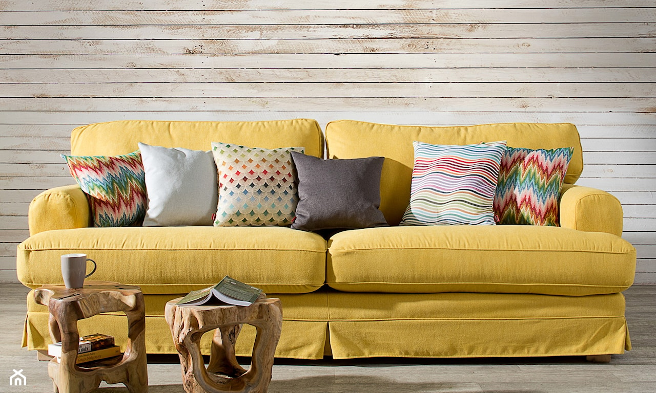 żółta sofa, drewniane panele na ścianie, drewniany stolik kawowy, kolorowe poduszki dekoracyjne