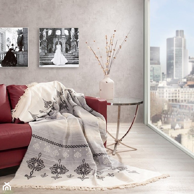 sofa z czerwonej skóry, biały wazon, szara ściana z betonowej masy, kremowy koc z czarnymi wzorami