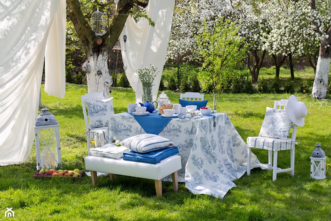białe krzesła w kwitnącym ogrodzie, białe zasłony, biało-niebieski obrus