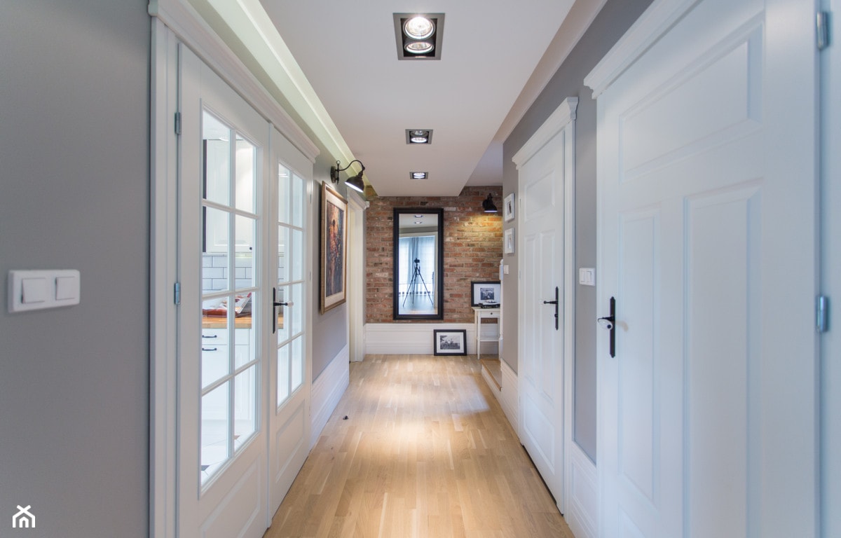 korytarz w stylu nowoczesnym, ceglana ściana, podłoga z jasnego drewna, białe drzwi