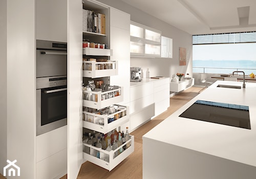 Oszczędzanie miejsca w kuchni - Średnia z salonem biała szara z zabudowaną lodówką z podblatowym zlewozmywakiem kuchnia z wyspą lub półwyspem z oknem, styl nowoczesny - zdjęcie od Blum