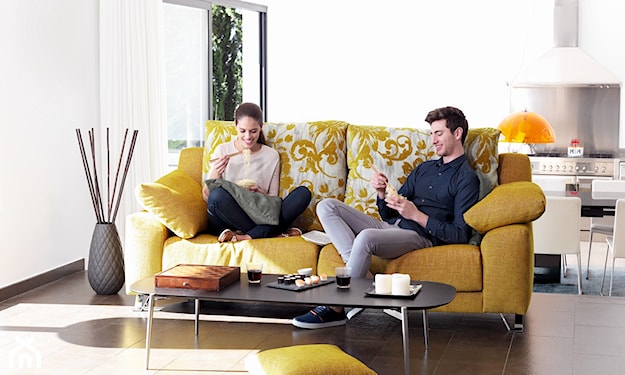 żółta sofa, stolik z czarnym blatem i metalowymi nóżkami, beżowe poduszki z żółtymi wzorami