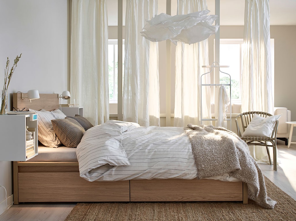 kremowe zasłony w sypialni, drewniana rama łóżka, wiklinowy fotel, beżowa narzuta, 