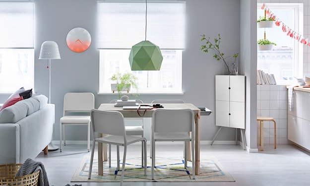 lampa wisząca z zielonym abażurem, stół z jasnego drewna, białe krzesła, biała szafka narożna, biała lampa podłogowa