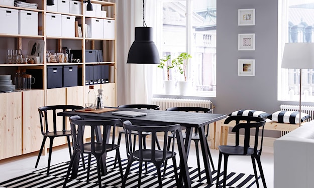 czarny stół i krzesła, dywanik w biało-czarne pasy, czarna lampa wisząca, drewniany regał