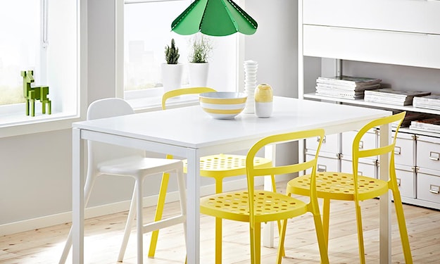 biały stół, zielona lampa wisząca, żółte krzesła, podłoga z jasnego drewna