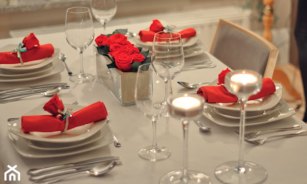 biały obrus na stole, czerwone serwetki, szklane świeczniki