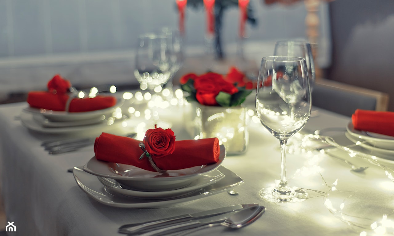 białe talerze, czerwona serwetka, lampki świąteczne na stole