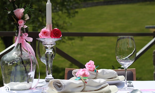 szklany świecznik, biały obrus, biała zastawa, różowe dekoracje stołu