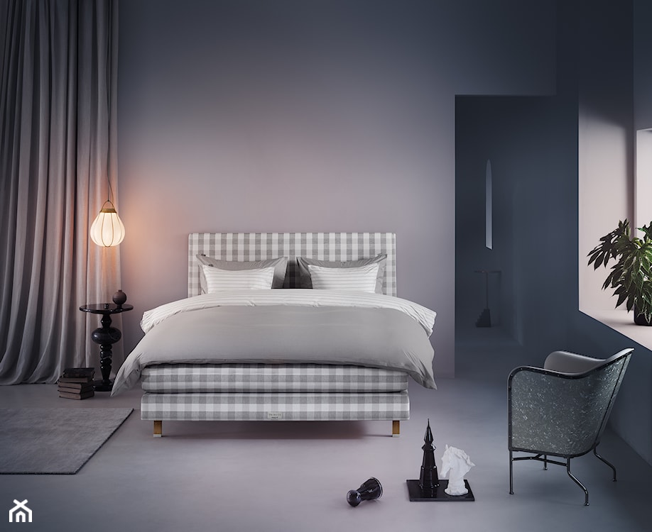 łóżko w szarą kratę Hästens, szara podłoga, szare ściany, okrągły stolik