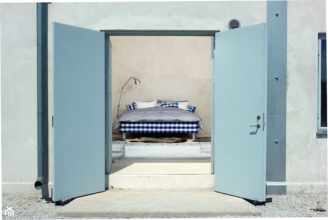 srebrna pościel, łóżko w biało-granatową kratę, metalowa lampa podłogowa, beżowa ściana