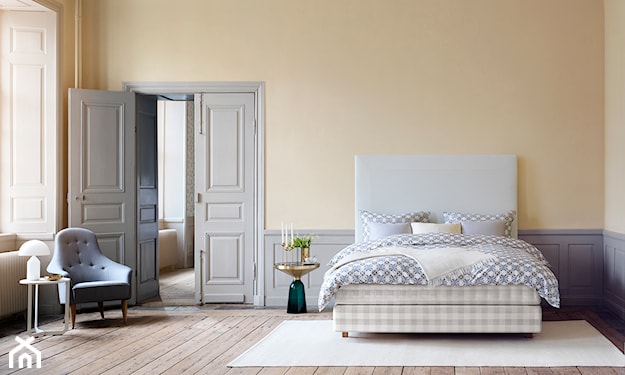 łóżko Hästens, kremowy dywan, białe drzwi dwuskrzydłowe, drewniana podłoga, żółte ściany