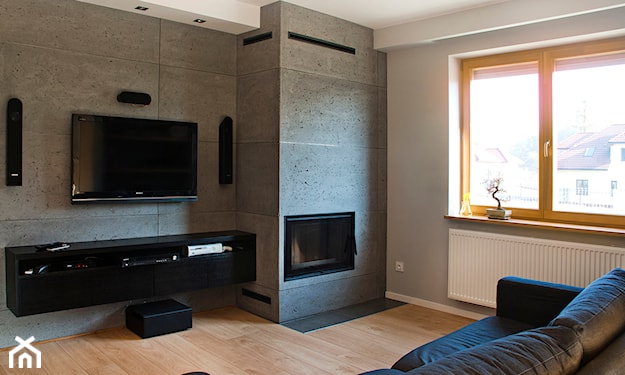 czarna sofa, drewniana podłoga, ściana z płyt betonowych, kominek w salonie