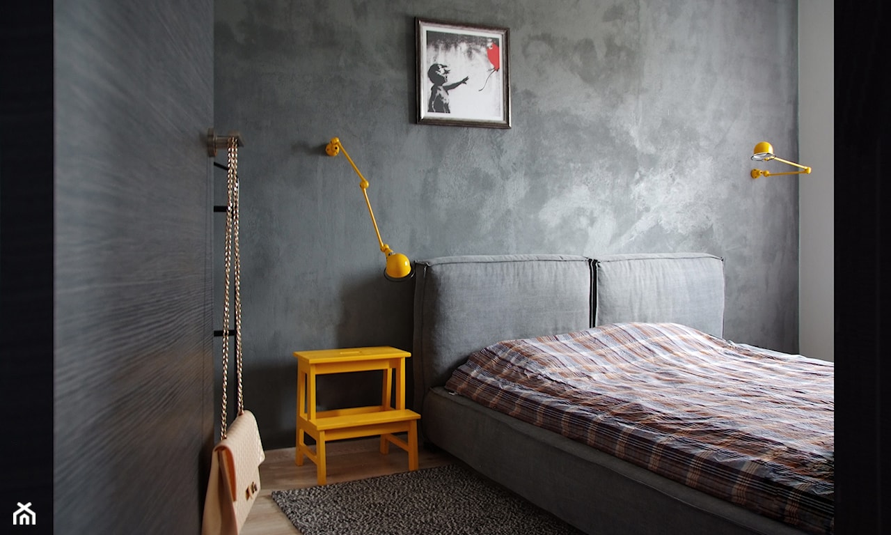 betonowa ściana w sypialni, żółte lampy nocne, szare łóżko tapicerowane